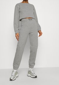 Felpa grigia corta con tre bottoni al colletto, abbinata a pantaloni della tuta grigi e sneaker argento metallico.