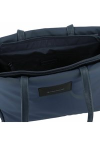 Sac fourre-tout bleu marine en matériau synthétique lisse, avec fermeture zippée et accents en cuir. Il dispose d'un intérieur spacieux avec une doublure noire.