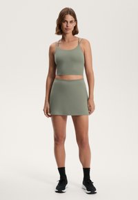 Zeleni crop top s tankimi naramnicami, v kombinaciji z usklajenim fitted krilom. Gladka tekstura tkanine, minimalistična zasnova in brez vidnih vzorcev.