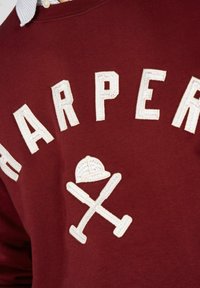 Sudadera burdeos con el texto bordado en blanco "HARPER" y un gráfico de una gorra cruzada con bate. Material de algodón, diseño de cuello redondo.