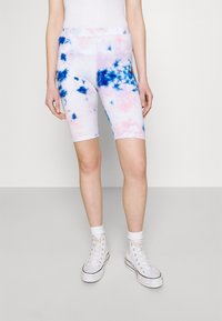 Bílé cyklistické šortky s růžovým a modrým tie-dye vzorem, s vysokým pasem a úzkým střihem. Nosené s bílými teniskami s vysokým kotníkem.