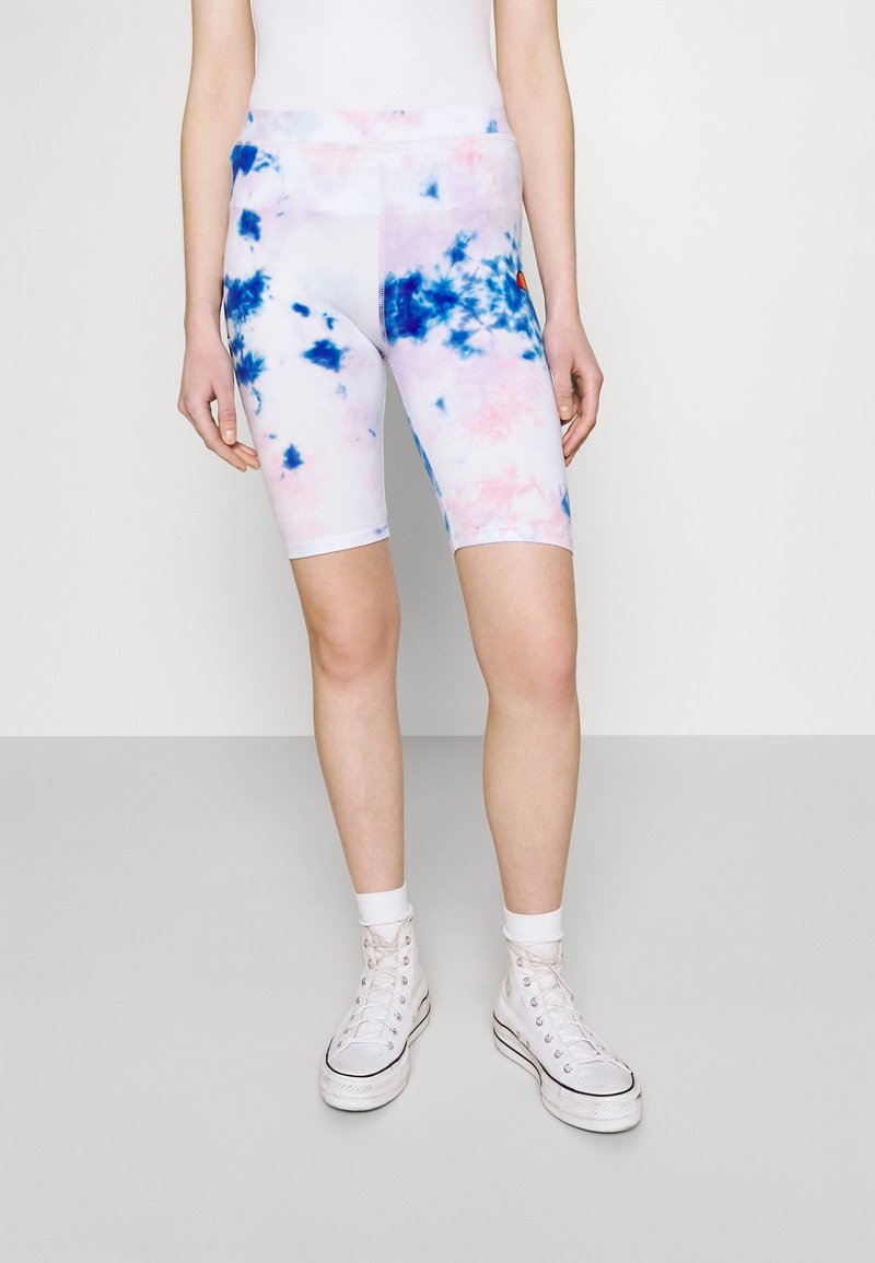 Bílé cyklistické šortky s růžovým a modrým tie-dye vzorem, s vysokým pasem a úzkým střihem. Nosené s bílými teniskami s vysokým kotníkem.