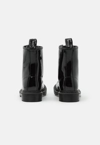 Botas de tobillo de charol negro con un acabado suave, punta redonda, suela de goma y pestañas negras en la parte posterior con texto blanco.