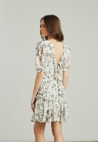 Blumenkleid mit kurzen Puffärmeln, gerafftem Saum und offener Rückseite. Leichter Stoff in Creme mit grünen und rosa Blumenmustern.