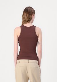 Brun, tettsittende tanktopp med rund hals og uten ermer, laget av glatt materiale, paret med beige skræddersydde bukser.