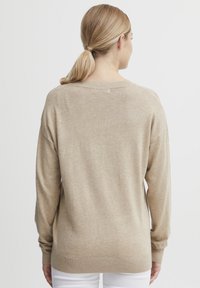 Beige hosszú ujjú pulóver, bordázott mandzsettával és laza szabással. Puha tapintás, széles nyakvonal, minimalista dizájn, és nincs látható minta.