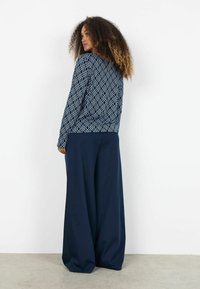 Námornícky vzorovaný sveter s geometrickými motívmi, skombinovaný s voľnými námorníckymi nohavicami. Materiál pôsobí mäkko a textúrovaný.