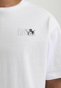 Hvid bomulds t-shirt med et lille grafisk motiv af en hund og teksten "PARK LIFE" i grå og sort. Blød tekstur med en afslappet pasform.