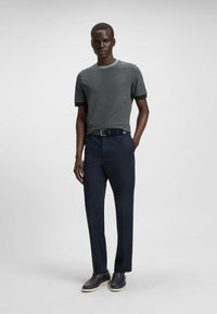 T-shirt grigio testurizzato da uomo con bande nere, abbinato a pantaloni blu navy. Completato da scarpe nere con suola chiara.