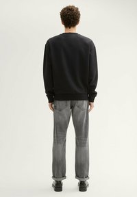 Czarny sweatshirt z prążkowanym dekoltem i mankietami, w połączeniu z szarymi, lekko przetartymi spodniami typu straight-leg oraz czarnym obuwiem.