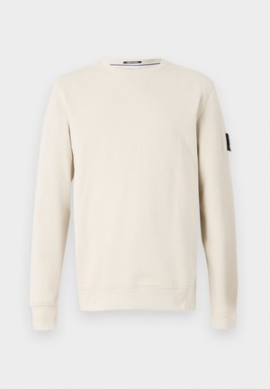 Sudadera de cuello redondo beige hecha de un tejido suave, con mangas largas y un pequeño logo negro en la manga izquierda.