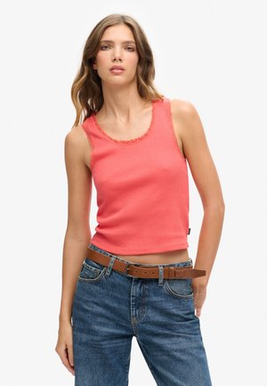 Koraal kleurige tanktop met kantafwerking, geribbelde textuur en ronde halslijn, gecombineerd met hoge taille blauwe spijkerbroek en een bruine riem.