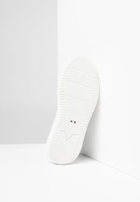 Weiße Sneaker-Sohle mit strukturierten Gummimustern, versehen mit einem auffälligen Logo, einem "Made in Italy"-Etikett und einem dezenten italienischen Flaggenakzent.