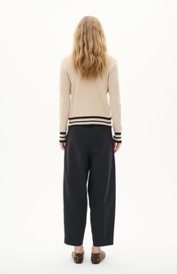 Pull en maille beige à côtes avec des accents rayés noirs aux poignets et à l'ourlet, associé à un pantalon noir ample et des chaussures à enfiler à imprimé léopard.