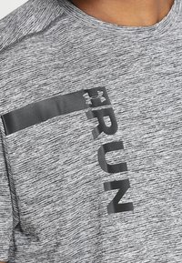 Maglietta atletica grigia con tessuto testurizzato; presenta la scritta 'RUN' nera e il logo su una striscia riflettente attraverso il petto.