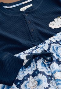 Haut côtelé bleu marine avec trois boutons, présentant un petit personnage blanc sur la poitrine, associé à un pantalon à motifs bleu et blanc avec un cordon de serrage.