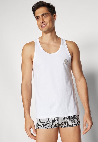 Top de algodón blanco sin mangas con un escote redondo, que presenta un pequeño logotipo bordado en el pecho, combinado con pantalones cortos de baño negros con estampado.