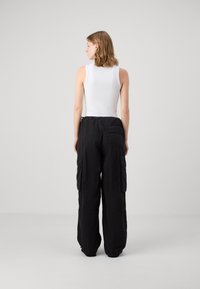 Vit ärmlös bodysuit i kombination med löst sittande svarta cargobyxor med stora sidofickor och dragsko i midjan.