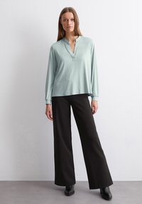 Maglia azzurro chiaro a maniche lunghe con colletto alla coreana, abbinata a pantaloni neri larghi, con una texture di tessuto liscia e una silhouette rilassata.