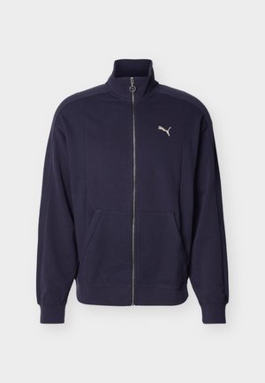 Tmavomodrá športová bunda na zips s vysokým golierom, bočnými vreckami, rebrovanými manžetami a bielym logom Puma na hrudi.