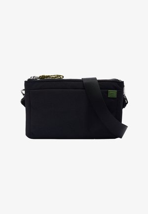 Czarna torba na ramię z tkaniny z zamkiem na suwak, ozdobiona zieloną naszywką z logo, regulowanym paskiem i teksturowanym wykończeniem.