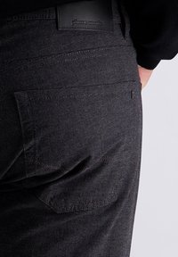 Zwarte gemusterde broek met een gladde textuur, voorzien van een achterzak en een leren label met de merknaam, Pierre Cardin, erin gedrukt.