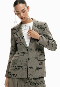 Hall triiksärkjakk musta käsitsi kirjutatud tekstiprintidega, kahe esitasku ja ühe nupuga sulgemisega. Sile kangas tugeva kujuga.