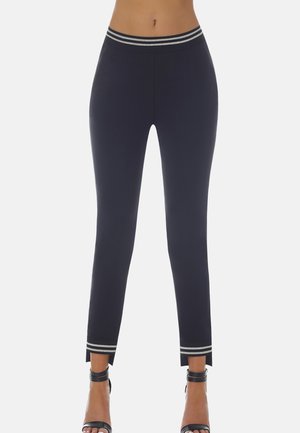 Kobieta ubrana w czarne, dopasowane spodnie z srebrzystym paskiem i mankietami w paski, połączone z czarnymi szpilkami z paskiem wokół kostki.