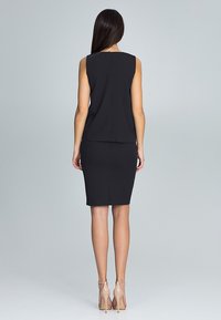 Zwart mouwloos topje gecombineerd met een aansluitende zwarte kokerrok. Glad materiaal, lengtemaat tot de knie, subtiele achterkantnaad en huidskleurige enkelbandhakken.