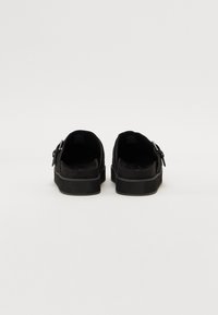 Crne slip-on cipele s teksturiranim gornjim dijelom, s okruglim vrhom i malim metalnim kopčama s obje strane.