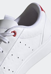 Vit sneaker med en slät, syntetisk ovandel med präglade hjärtmotiv. Röda öglor, vita snören och en vadderad krage för komfort.