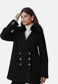 Čierny dvojradový kabát so zlatými gombíkmi, umelá kožušina na golieri, prispôsobený strih a dlhé rukávy. Obsahuje dve predné vrecká.