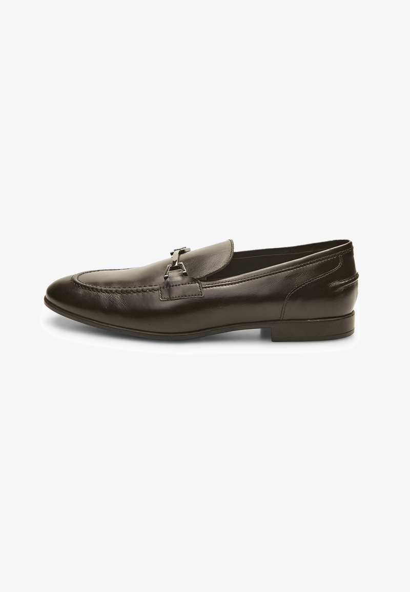 Mocassin homme en cuir noir avec détail en métal argenté et petit talon, vu de profil sur fond blanc.