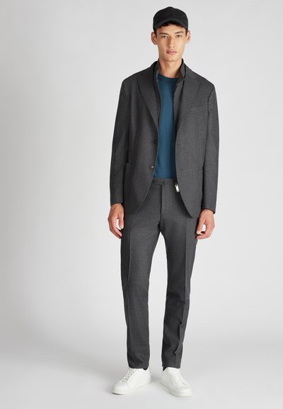 Giacca su misura grigia con pantaloni coordinati, indossata sopra una camicia blu. Sneakers bianche completano l'outfit. Tessuto liscio, design strutturato.