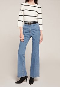 Vit och svart randig långärmad topp med vågig ringning, kombinerad med högmidjade ljusblå utsvängda jeans och svarta spetsiga klackar.