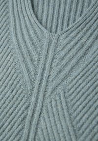 Hellblau gestrickter Pullover mit V-Ausschnitt, der über strukturierte Rippstrickmuster und Zickzackdesigns verfügt. Der Stoff wirkt weich mit einem leicht melierten Finish.