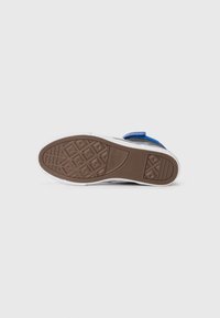 Fäste sneakers med blå accent, vit ovandel och en texturerad brun gummisula med geometriska mönster.