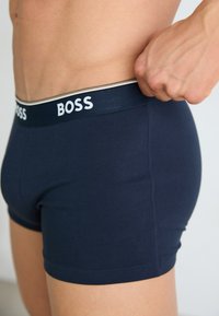 Temno modri bokserji z gladko teksturo, z belim logotipom "BOSS" na elastičnem pasu in prilegajočim dizajnom.