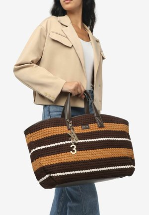 Grand sac fourre-tout avec des rayures entrelacées brunes, beiges et blanches. Dispose de poignées en cuir marron foncé et d'un charme décoratif avec le numéro 3.