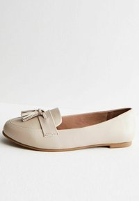 Beige leather loafer with rounded toe, decorative tassel detail, and flat rubber sole. Smooth texture and minimalistic design.