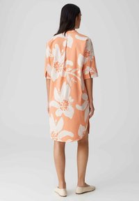 Bloemen midi-jurk van zacht perzikkleurig stof, met witte bloemenpatronen, korte mouwen, zijsplitsen en een ontspannen pasvorm.