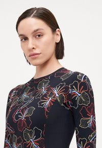 Maillot de bain noir avec un motif floral en rouge, jaune et bleu. Présente un design ajusté et des manches longues, fabriqué en tissu extensible.