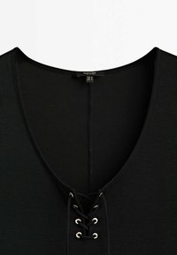 Haut en tissu côtelé noir avec décolleté en V et détail à lacets avec des cordons noirs passant à travers des œillets argentés.