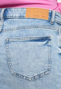 Ανοιχτό μπλε τζιν παντελόνι με πίσω τσέπη, που διαθέτει ταμπέλα από δέρμα καφέ χρώματος με την επιγραφή «NOIS MAY». Ομαλή υφή και κλασικός σχεδιασμός τζιν.