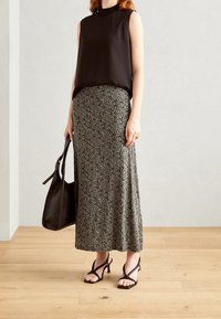 Haut sans manches noir associé à une jupe à motif de longueur cheville dans des tons de noir et de crème ; le modèle tient un sac à main noir et porte des talons à lanières.