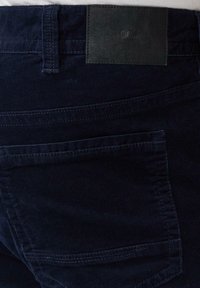 Donkerblauwe corduroy broek met een achterzak, een ceintuurlus en een zwart leren merkplaatje gestikt boven de zak.