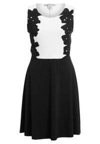 Robe noire et blanche avec un corsage ajusté orné d'accents en dentelle florale sur les épaules, et une jupe noire évasée. Texture de tissu lisse.