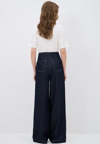 Korkeavyötäröiset, leveälahkeiset siniset farkut, joissa on viisi taskua ja valkoiset ompelusaumat, yhdistettyinä yksinkertaiseen valkoiseen t-paitaan.