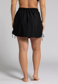 Falda de baño negra con cinturilla elástica y cuerdas ajustables a los lados, textura suave y longitud hasta medio muslo.