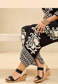 Schwarz-weiß gemustertes Outfit mit weitem Bein und klobigen schwarzen Wedgesandalen mit Korksohle und elastischen Riemen.